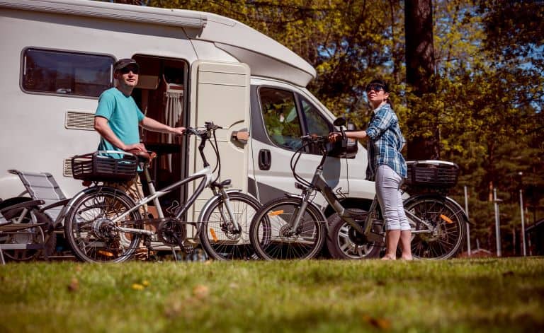 Man and a woman on e-bikes resting next to an RV